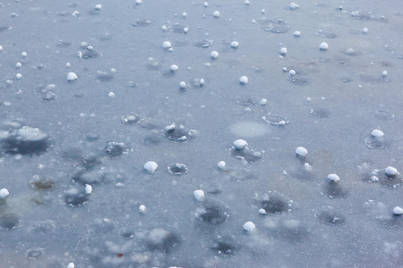 Close-up view of frozen hailstones scattered on icy pavement, showcasing winter weather phenomena.